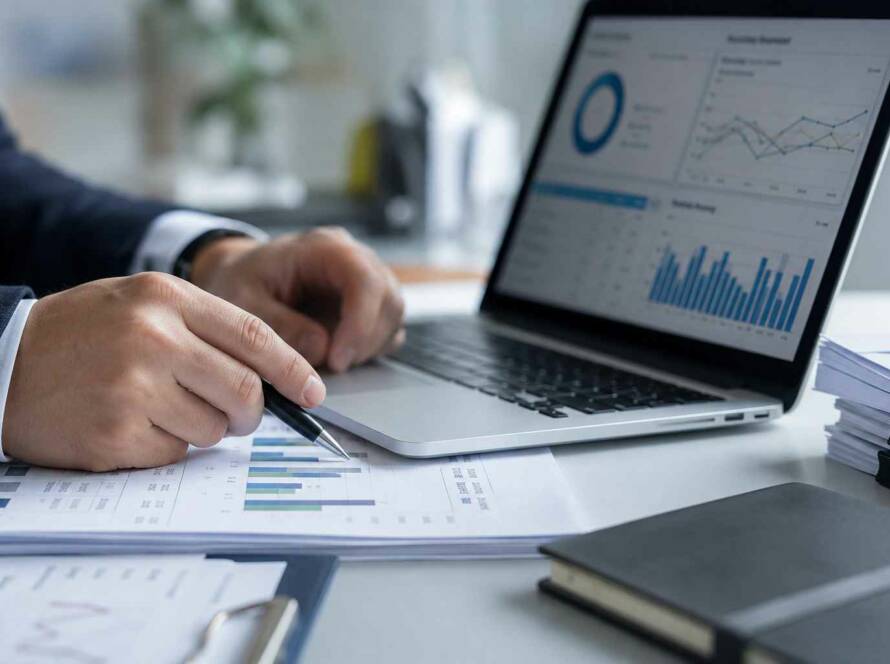 Un professionnel de la finance analyse des graphiques de performance sur un ordinateur portable et des documents imprimés pour structurer une approche par les risques en LCB-FT.