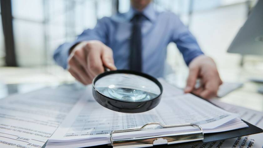 Un professionnel de la finance ou du droit utilisant une loupe pour examiner minutieusement des documents sur un bureau, illustrant un processus de due diligence renforcée.