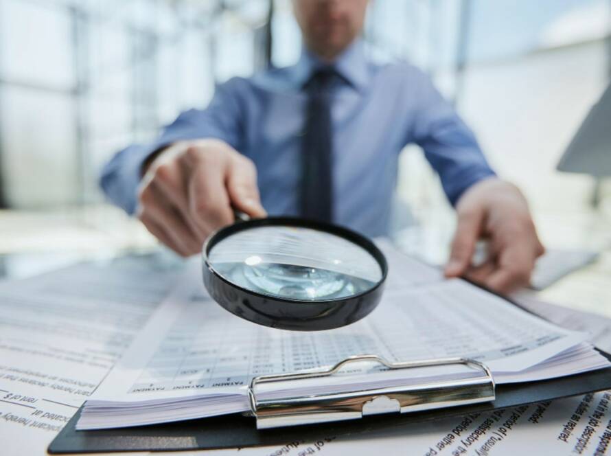 Un professionnel de la finance ou du droit utilisant une loupe pour examiner minutieusement des documents sur un bureau, illustrant un processus de due diligence renforcée.
